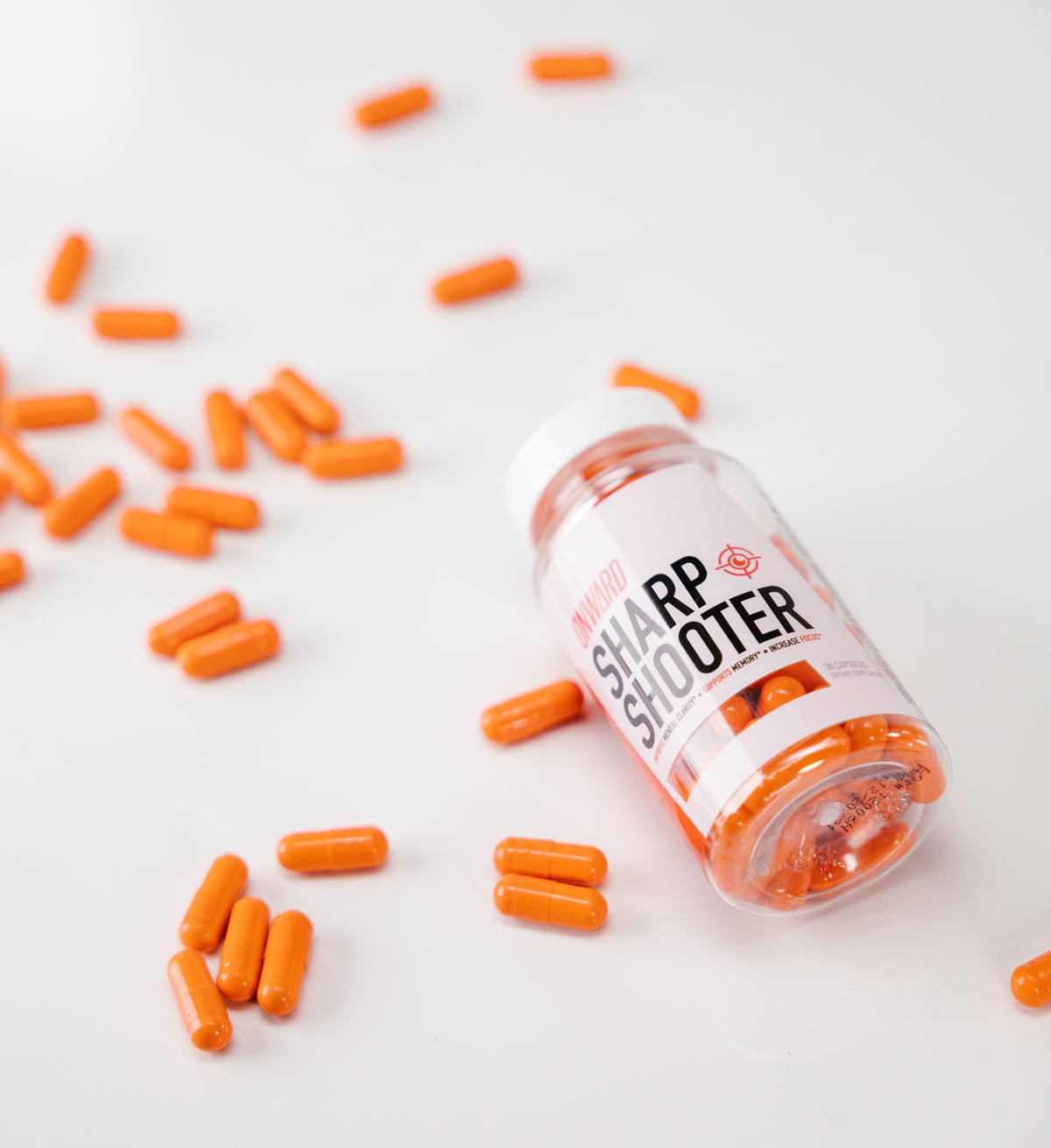 A clear bottle of Onward lies on its side agains a white background with orange capsules scattered.